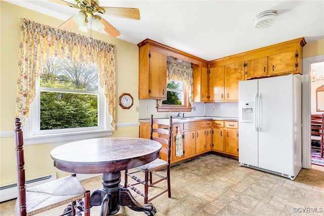 kitchen featuring brown cabinets, stone finish floor, white fridge with ice dispenser, a ceiling fan, and a baseboard radiator