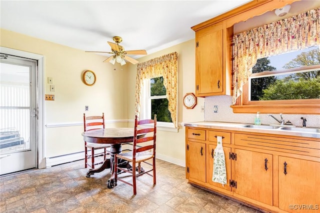kitchen featuring stone finish floor, a ceiling fan, backsplash, a sink, and light countertops