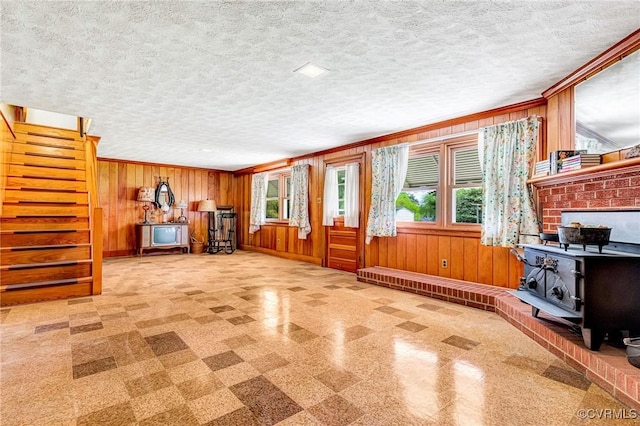 unfurnished living room featuring stairs, crown molding, wood walls, and a wood stove