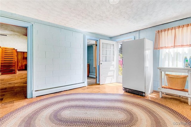 unfurnished bedroom with freestanding refrigerator, concrete block wall, a textured ceiling, and baseboard heating