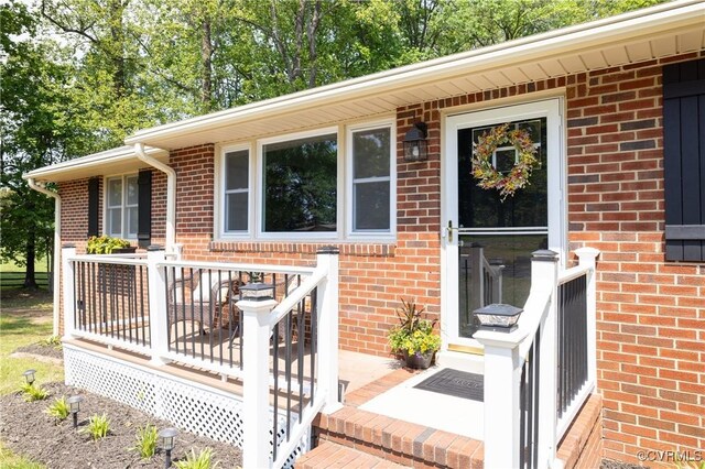 view of exterior entry featuring brick siding and a deck