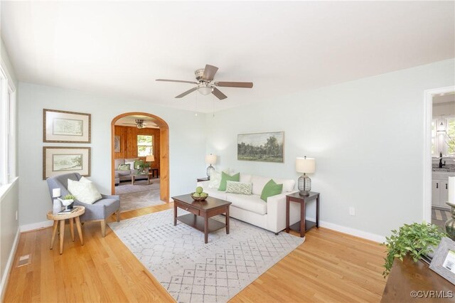 living area with arched walkways, a ceiling fan, plenty of natural light, and baseboards