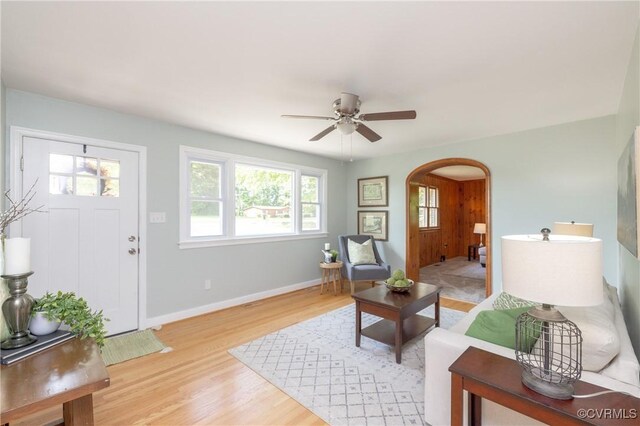 living room with arched walkways, ceiling fan, a healthy amount of sunlight, and light wood-type flooring