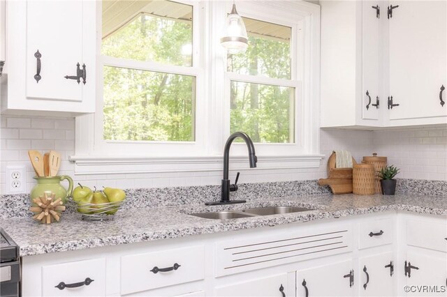 kitchen with decorative light fixtures, tasteful backsplash, a sink, light stone counters, and white cabinetry