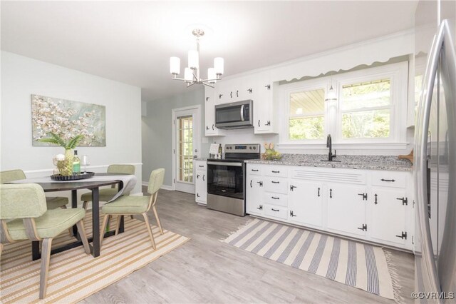 kitchen with a chandelier, white cabinets, a sink, light wood-style flooring, and appliances with stainless steel finishes