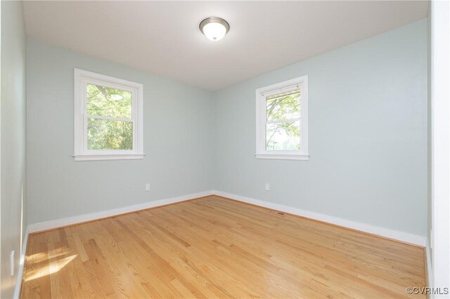 unfurnished room featuring plenty of natural light, baseboards, and wood finished floors