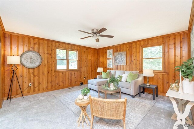 carpeted living room with wooden walls, ceiling fan, and a healthy amount of sunlight