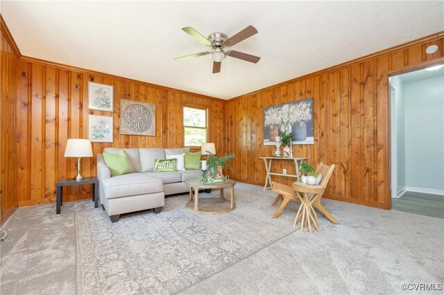 carpeted living area with crown molding, a ceiling fan, baseboards, and wood walls