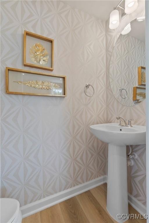 half bathroom with baseboards, wood finished floors, and toilet