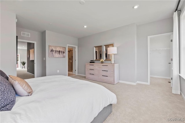 bedroom with visible vents, baseboards, a walk in closet, and light colored carpet