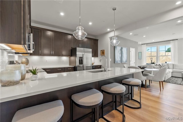 kitchen with dark brown cabinetry, a sink, light countertops, open floor plan, and stainless steel appliances