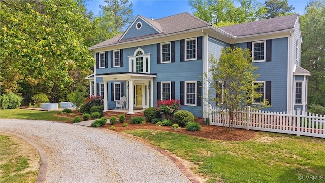 colonial inspired home with a front lawn, fence, and gravel driveway