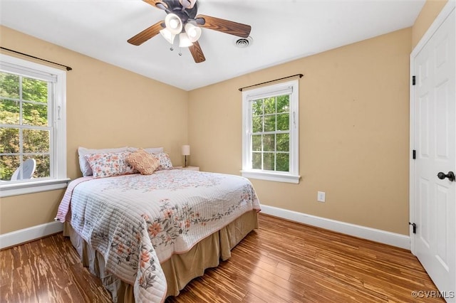 bedroom with baseboards, multiple windows, and wood finished floors