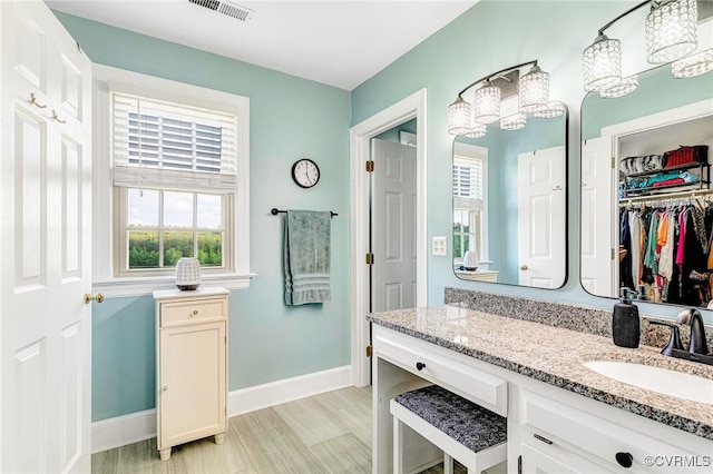 bathroom featuring visible vents, vanity, baseboards, a spacious closet, and a notable chandelier