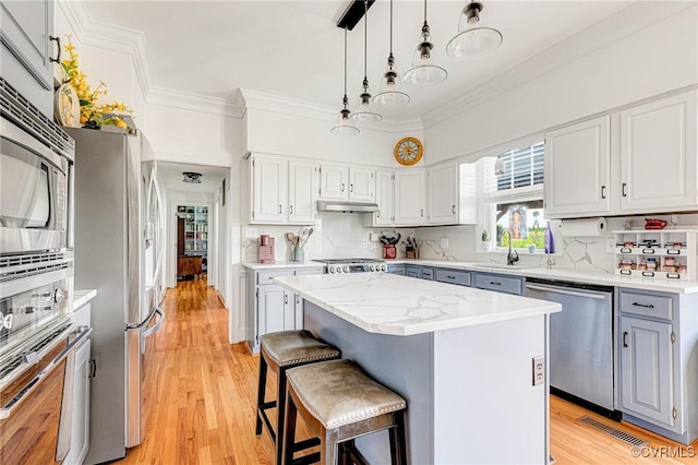 kitchen with a kitchen island, pendant lighting, appliances with stainless steel finishes, a sink, and ornamental molding