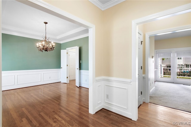 unfurnished dining area featuring crown molding, an inviting chandelier, dark wood-style floors, and a wainscoted wall