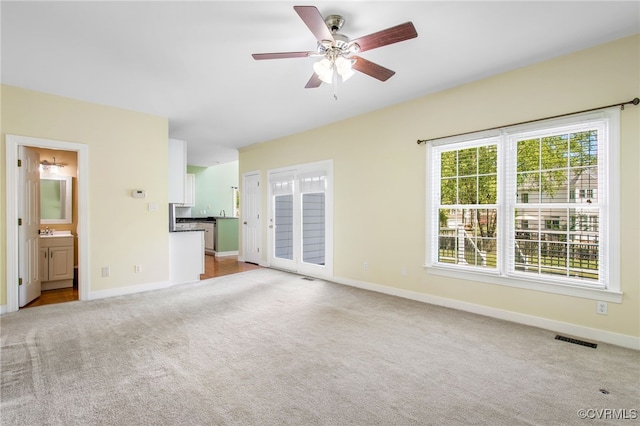 unfurnished living room with a ceiling fan, visible vents, a sink, carpet floors, and baseboards