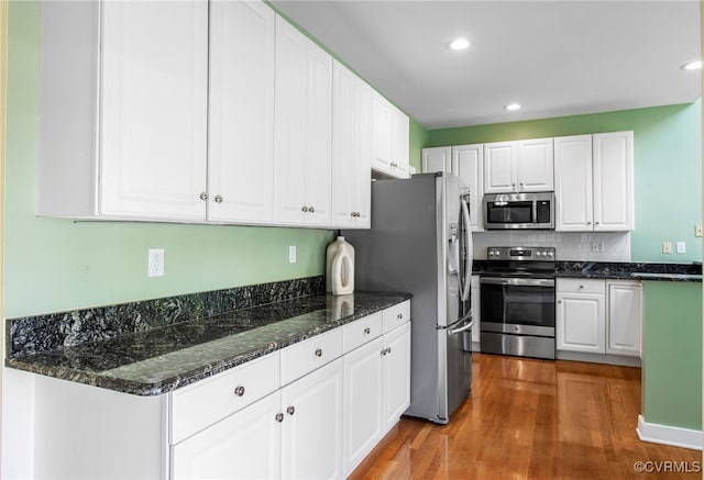 kitchen with decorative backsplash, wood finished floors, white cabinets, dark stone countertops, and stainless steel appliances