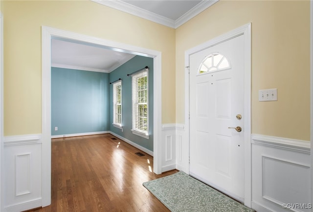 entrance foyer with crown molding, wainscoting, wood finished floors, and visible vents