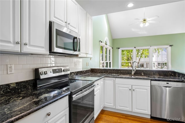 kitchen featuring decorative backsplash, vaulted ceiling, a sink, stainless steel appliances, and white cabinetry