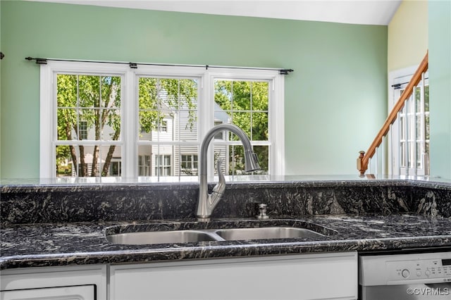 details with stainless steel dishwasher, a sink, dark stone countertops, and white cabinets