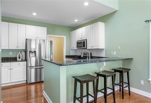kitchen with dark stone counters, appliances with stainless steel finishes, wood finished floors, and white cabinets