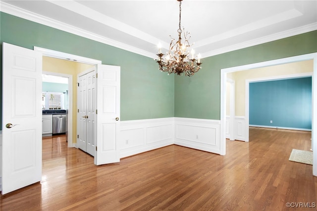 unfurnished dining area featuring an inviting chandelier, a raised ceiling, crown molding, and wood finished floors