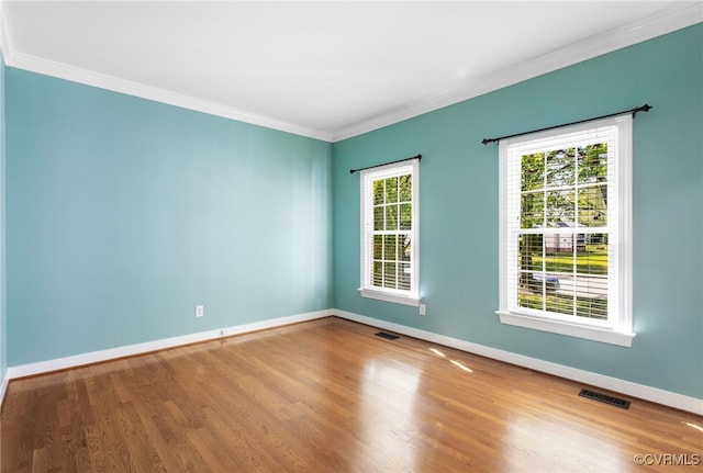 empty room featuring crown molding, baseboards, wood finished floors, and visible vents