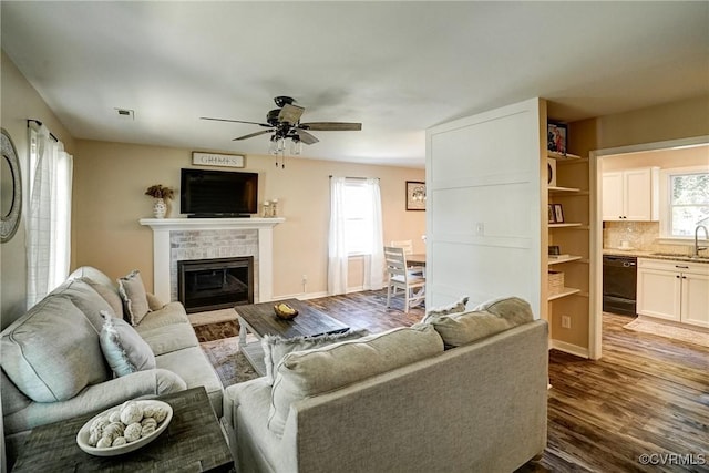 living room featuring dark wood-style flooring, a ceiling fan, a brick fireplace, and baseboards