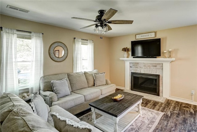 living area featuring a ceiling fan, a brick fireplace, wood finished floors, and baseboards