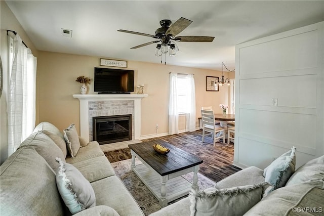 living area featuring a chandelier, baseboards, wood finished floors, a ceiling fan, and a brick fireplace