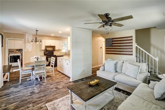 living area with dark wood-style floors, stairway, a chandelier, a ceiling fan, and baseboards