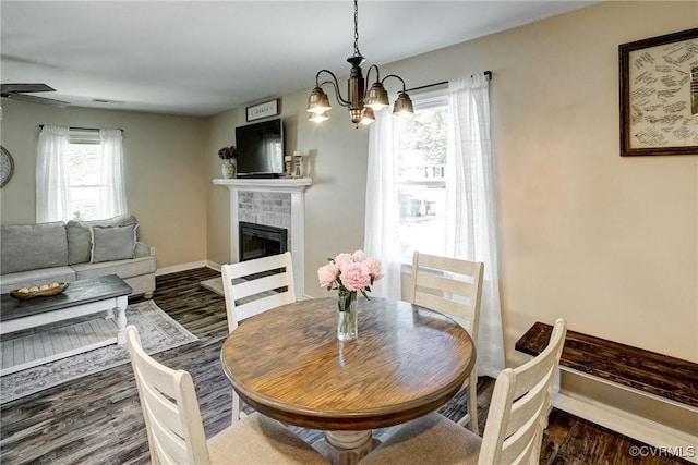 dining room featuring a brick fireplace, wood finished floors, a chandelier, and baseboards