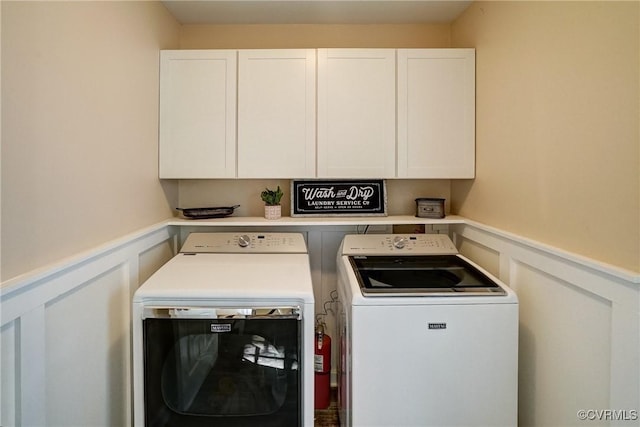 washroom with cabinet space, washer and clothes dryer, a decorative wall, and a wainscoted wall