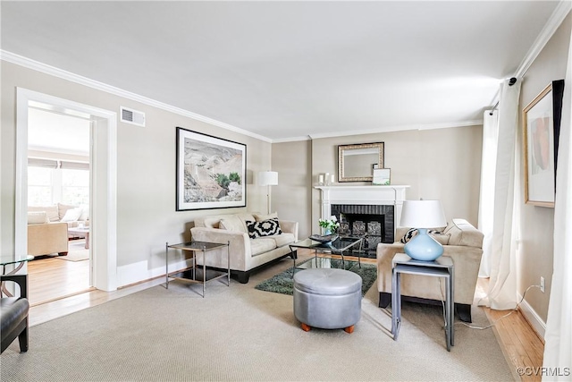 living area featuring a brick fireplace, baseboards, wood finished floors, visible vents, and ornamental molding
