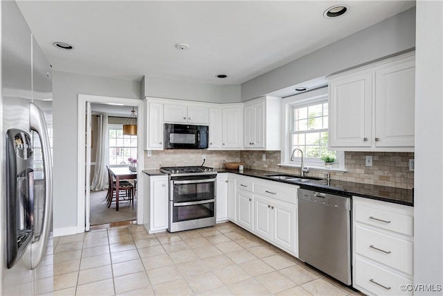 kitchen with a sink, appliances with stainless steel finishes, dark countertops, and white cabinetry