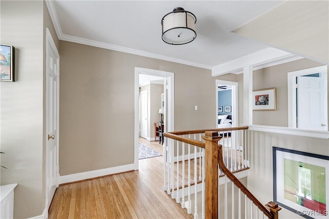 hallway featuring light wood-type flooring, baseboards, crown molding, and an upstairs landing
