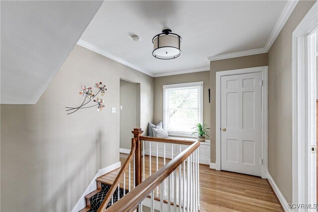 corridor with baseboards, an upstairs landing, ornamental molding, and light wood-type flooring