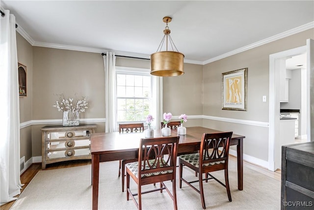 dining area featuring crown molding, baseboards, and light wood-style flooring