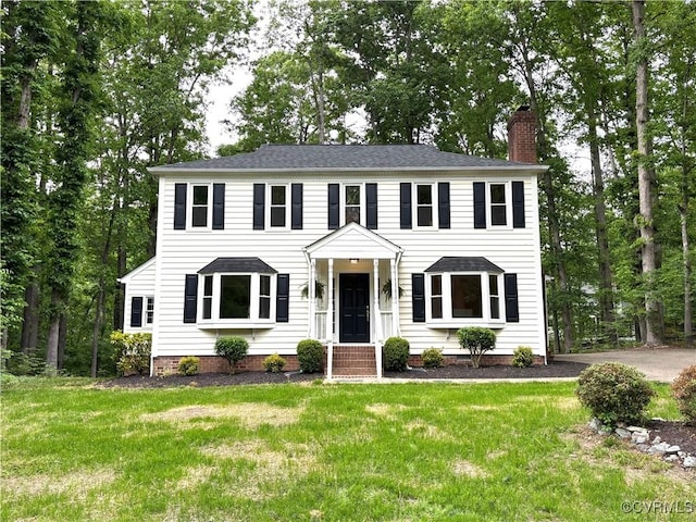 colonial inspired home featuring a chimney, a front yard, and a shingled roof