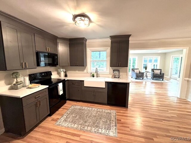 kitchen with black appliances, a sink, crown molding, light wood-style flooring, and light countertops
