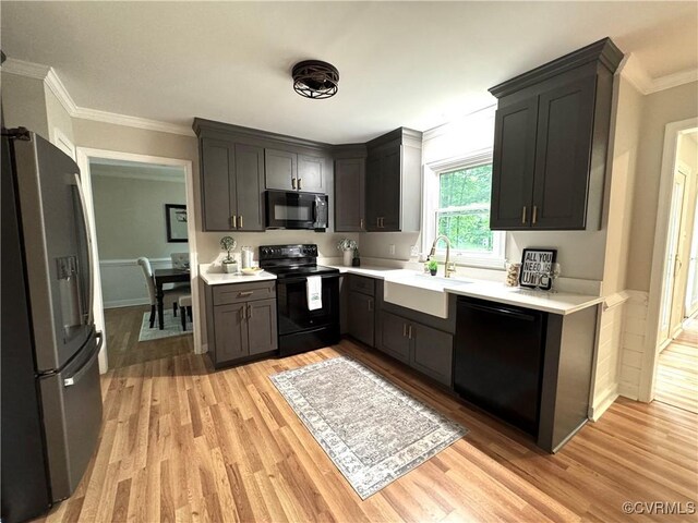 kitchen featuring black appliances, a sink, light wood-style flooring, light countertops, and crown molding