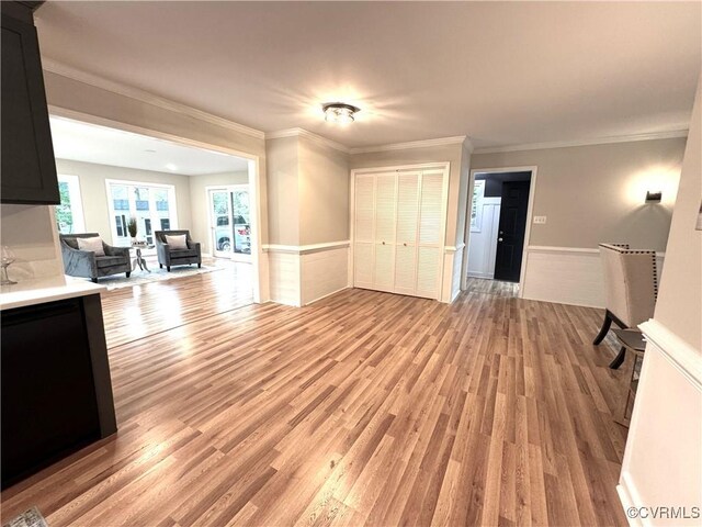 unfurnished living room with light wood finished floors, a wainscoted wall, and ornamental molding