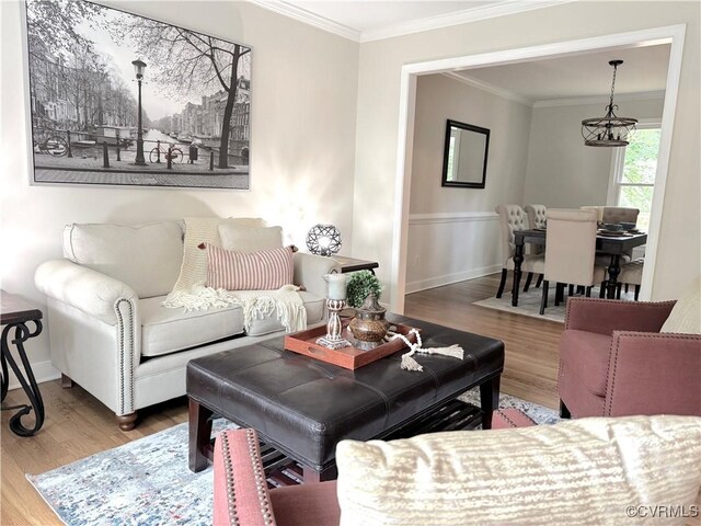 living room with wood finished floors, ornamental molding, a chandelier, a wainscoted wall, and baseboards