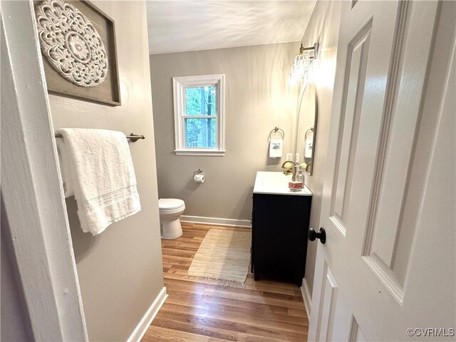 half bath with baseboards, wood finished floors, toilet, and vanity
