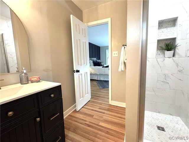 ensuite bathroom featuring baseboards, wood finished floors, a tile shower, and vanity