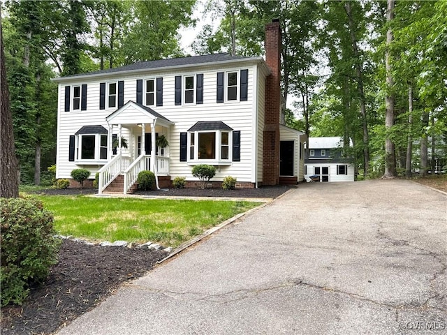 colonial home featuring a chimney and asphalt driveway