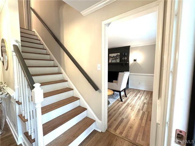 stairs with crown molding and wood finished floors