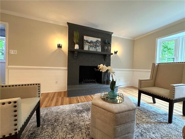 living room with plenty of natural light, wainscoting, wood finished floors, crown molding, and a brick fireplace