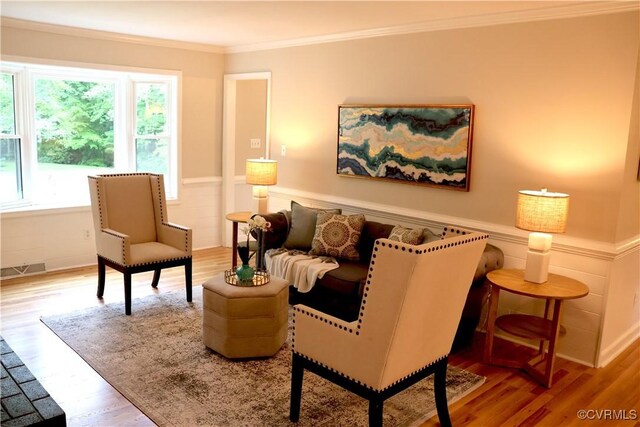 sitting room with plenty of natural light, crown molding, wood finished floors, and wainscoting